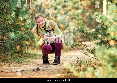 Mädchen im Freien mit einem kleinen Hund. lächelnde Mädchen mit Hund. schöne Mädchen in einer Jacke und Kappe mit dem kleinen Hund ein Chihuahua Welpen. Kind lächelnd Stockfoto