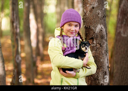 Baby Mädchen im Freien mit einem kleinen Hund. lächelnd Jugendmädchen entspannen mit Hund. cute Teen Girl trägt eine Jacke und lila Hut, Wandern mit ihrem Chihuahua Stockfoto