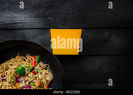 Udon fry Nudeln mit Huhn und Gemüse im Wok rühren Pan auf schwarzem Holz- Hintergrund. Mit einer Box für Nudeln. nach oben anzeigen. Stockfoto