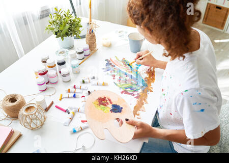 Hohen winkel Portrait von inspiriert junge Frau Malerei schönen Öl Bild am Schreibtisch sitzen in kleinen Art Studio Stockfoto