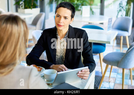 Portrait von erfolgreichen elegante Geschäftsfrau hören auf Partner mit digitalen Tablet besprechen sie bei der Arbeit während der Sitzung im Cafe Stockfoto