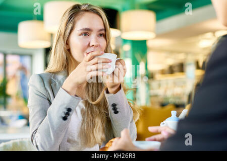 Porträt der moderne junge Frau trinkt Kaffee im Cafe Tabelle zu jemand sitzt ihr Gegenüber hören Stockfoto
