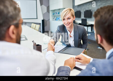 Portrait der Junge erfolgreiche Geschäftsfrau Händeschütteln mit Partnern in der Sitzung Tabelle im Board Room nach erfolgreicher Deal Stockfoto