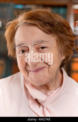 Portrait von lächelnden älteren Frau. Selektive konzentrieren, auf Defokussierten Bücherregal Hintergrund Stockfoto