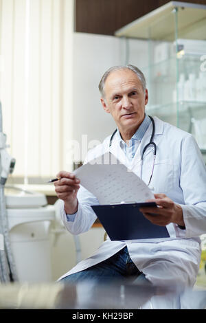 Hausarzt in Uniform, der in Kliniken medizinische Papiere durchsucht Stockfoto