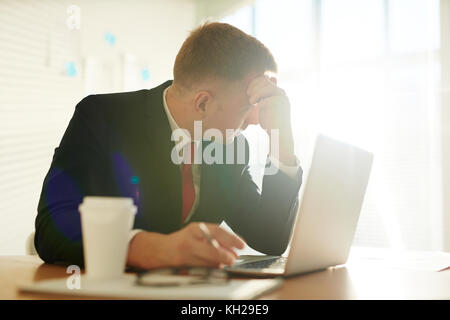 Ein Geschäftsmann, der vor dem Laptop sitzt und über Ideen im Büro nachdenkt Stockfoto