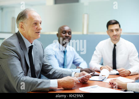 Drei interkulturelle Geschäftsleute in Formalwear arbeiten bei Meetings, hören sich Finanzberichte an und diskutieren neue Strategien Stockfoto