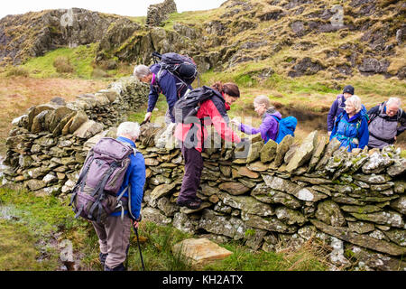 Ramblers Gruppe klettern Stein Stil über Trockenmauer auf dem Weg bis Jahre Aran Berg in Snowdonia National Park. Gwynedd, Wales, Großbritannien, Großbritannien Stockfoto