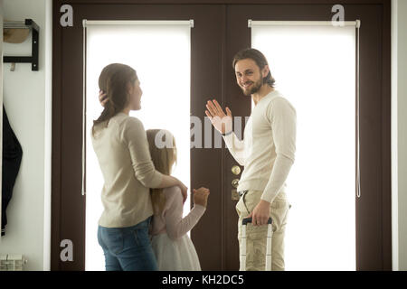 Mutter und Tochter sehen Sie Vater für Geschäftsreise, Mama mit Kind Mädchen Abschied von Papa winkende Hand stehend zu Hause Tür Holding tra verlassen Stockfoto