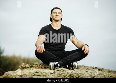 Mann sitzt auf felsigen Strand in den Sonnenuntergang am Meer. Stockfoto