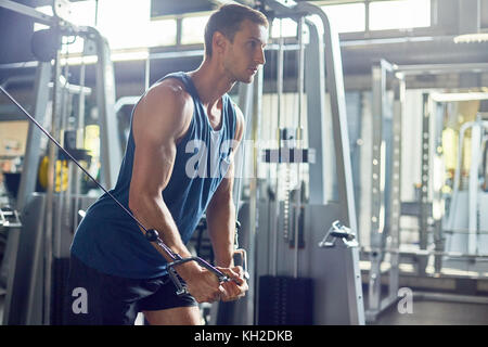 Seitenansicht Portrait von Stattlichen muskulösen Mann mit Maschinen im modernen Fitnessraum trainieren, kopieren Raum Stockfoto