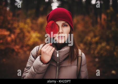 Porträt der Frau, die im Herbst Wald und deckt die Hälfte der ihr Gesicht mit Herbst Blatt. Stockfoto