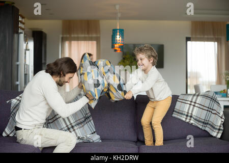 Kissenschlacht zwischen Vater und Sohn im Wohnzimmer, gerne Vater und Kind Junge spielt auf einem Sofa mit Kissen, Papa lachen Spaß haben w Stockfoto
