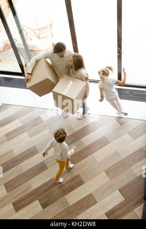 Familie und Kinder ziehen in ein neues Zuhause, Kinder, die herumlaufen, Eltern halten Kästen, die zusammen im Haus stehen, glückliches Paar mit zwei Chi Stockfoto