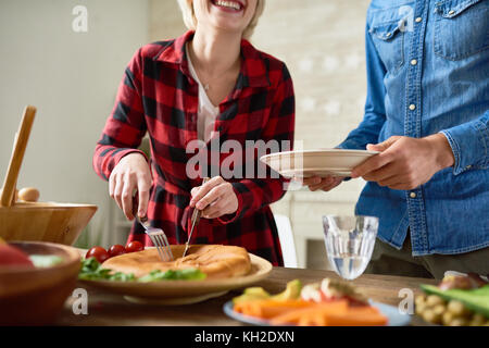 Den mittleren Abschnitt der unkenntlich junge Frau schneiden hausgemachte Kuchen am Tisch und servieren es Platten Stockfoto