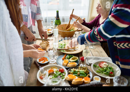 Im mittleren Abschnitt Gruppe junger Menschen die Vorbereitung Abendessen für festliche Feier am großen Tisch und Gerichte machen Stockfoto