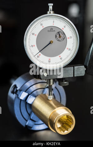 Toleranz Messung von Messing Werkstück in Chuck. anbringen und die Meßuhr in der Halterung auf dem schwarzen Hintergrund. Engineering, Bildung, Industrie Konzept. Stockfoto