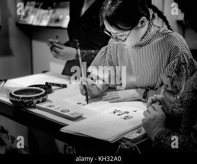 Eine schwarze und weiße horizontale Bild eines chinesischen Mädchen schreiben/zeichnen Kalligraphie im Klassenzimmer. Stockfoto