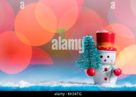 Schneemann Weihnachten Dekoration mit einer kleinen Kiefer, Schnee auf blauem Holz Oberfläche, mit Hintergrund bunte bokeh Lichter, blau und kalten Farbton Stockfoto