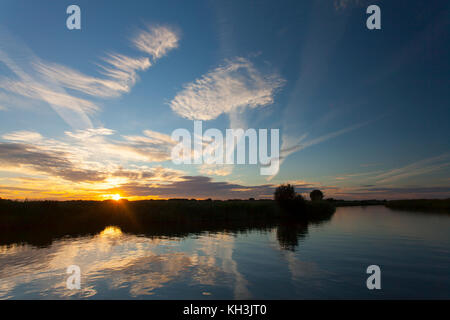 Sonnenuntergang auf Flotte Deich, in der nähe von South Walsham breit und des Flusses Bure auf der Norfolk Broads. hohe Wolken und Sonnenuntergang in Ruhe, noch Fluss Gewässer wider Stockfoto