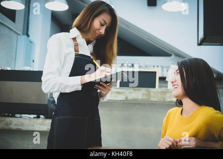 Jungen asiatischen Barista, um der Frau in dem Cafe. Cafe Restaurant Service, Inhaber kleiner Unternehmen, die Lebensmittel- und Getränkeindustrie. Stockfoto