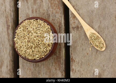 Hölzerne Schüssel mit Fenchel Samen und einem Löffel aus Holz mit Fenchel Samen über ein Holzdeck gefüllt Stockfoto