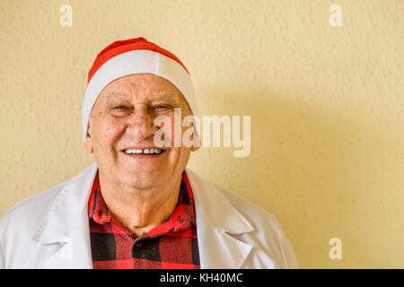 Alte Arzt mit weißem medizinischen Kleid und kariertem Hemd lächelnd und Tragen santa claus hat Stockfoto