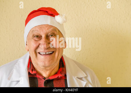 Alte Arzt mit weißem medizinischen Kleid und kariertem Hemd lächelnd und Tragen santa claus hat Stockfoto