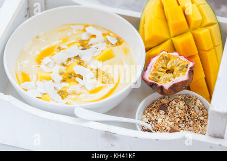 Mango smoothie Schüssel mit Kokosnuss, Müsli und Passionsfrucht in einem weißen Kasten. Gesunde vegane Ernährung frühstück Konzept. Stockfoto