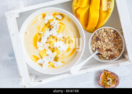 Mango smoothie Schüssel mit Kokosnuss, Müsli und Passionsfrucht in einem weißen Kasten. Gesunde vegane Ernährung frühstück Konzept. Stockfoto