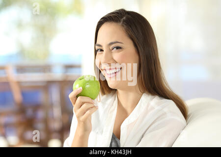 Porträt einer Frau, die eine gesunde green apple sitzt auf einem Sofa im Wohnzimmer zu Hause Stockfoto