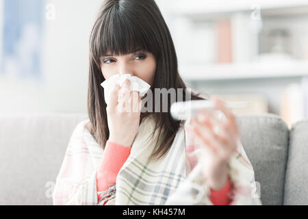 Junge kranke Frau mit Erkältung und Grippe, sie bläst ihre Nase und messen ihre Körpertemperatur Stockfoto