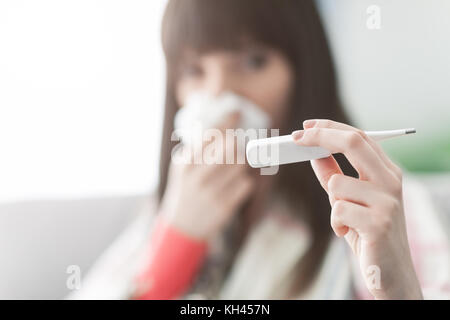 Junge kranke Frau mit Erkältung und Grippe, sie bläst ihre Nase und messen ihre Körpertemperatur Stockfoto