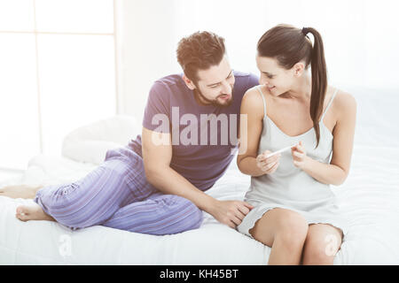 Junge Paar einen Schwangerschaftstest, sie sitzen zusammen im Bett und lächelnd Stockfoto