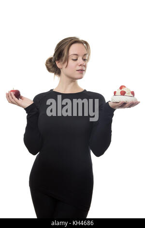 Fitness-Woam ganz in schwarz hält einen Apfel und Erdbeere Und Vanilla Pavlova, die eine Wahl macht, was man essen soll Stockfoto