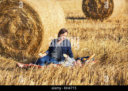 Glückliche Mutter und 2 Jahre alten Mädchen neben Heuballen in geernteten Feld Stockfoto