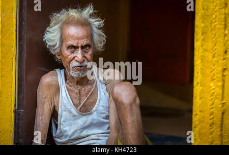 Nahaufnahme eines alten Mannes, der an seiner Tür sitzt, in einer Gasse in Varanasi, Indien. Stockfoto