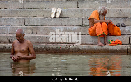 Varanasi Ganges ghat mit einem Sadhu Baba sitzt auf der Treppe und ein alter Mann in der Meditation im Wasser des Ganges. Stockfoto