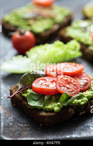 Toast mit Avocado, Spinat und Cherry Tomaten auf Vollkorn Roggenbrot. Detailansicht, selektiver Fokus Stockfoto