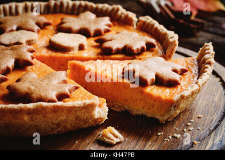 Kürbiskuchen mit Slice ausgeschnitten mit Lebkuchen maple leaf geformte Cookies auf holzbrett eingerichtet. Detailansicht Stockfoto