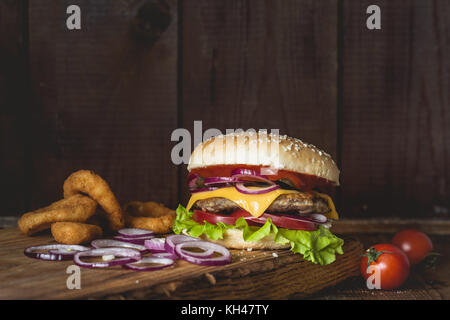 Cheeseburger und Zwiebelringe auf Holz Schneidebrett über Holz- Hintergrund. Detailansicht mit Platz für Text kopieren Stockfoto