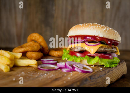 Cheeseburger, Pommes frites und Zwiebelringe auf Holz Schneidebrett über Holz- Kulisse. Horizontale, Detailansicht Stockfoto