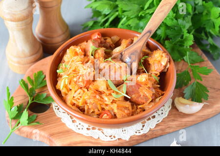 Gekochtes Sauerkraut mit Würstchen und Gewürze in einem traditionellen Schüssel auf einem hölzernen Hintergrund. gesundes Essen. Hausmannskost Stockfoto