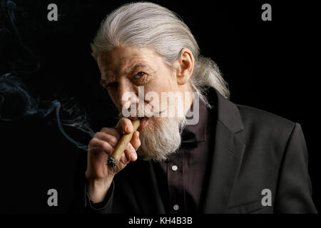 Stilvolle alter Mann mit langen grauen Haaren rauchen Zigarre. Stockfoto