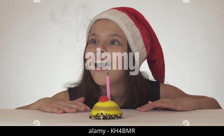 Schöne naughty girl Teenager in einem Santa Claus hat bläst eine Kerze auf eine festliche Kuchen auf weißem Hintergrund Stockfoto