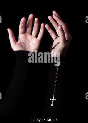 Weibliche Hände mit ausgestreckten Armen beten und Holding Rosenkranz mit Kreuz oder Kruzifix. schwarzer Hintergrund. Frau mit christlichen katholischen Hand glauben Stockfoto