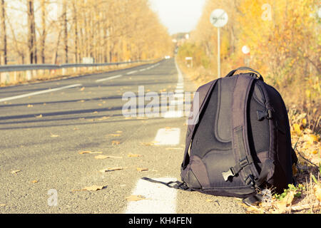 Rucksack auf der Seite der Straße als Travel Concept an einem sonnigen Tag im Herbst oder fallen Stockfoto