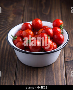 Red Cherry Tomaten in Weiß Emaille Schüssel auf Holz- Hintergrund Stockfoto