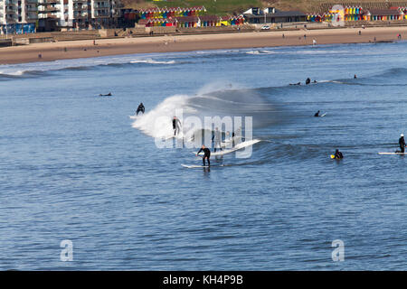 Surfer und paddleboarders im Norden der Bucht von Scarborough, Strand und bunten Beach Chalets können im Hintergrund gesehen werden. Stockfoto