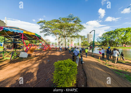 Kinder Fahrgeschäfte sowie Menschen zu Fuß durch Uhuru Park durch den See zum Bootfahren am späten Nachmittag Licht, Nairobi, Kenia Stockfoto